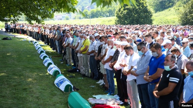 People pray near coffins at a graveyard during a mass funeral in Potocari near Srebrenica, Bosnia and Herzegovina July 11, 2020.