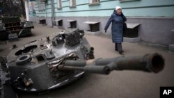A woman walks by a destroyed Russian tank put on display in a street in central Kyiv, Ukraine, Jan. 25, 2023.