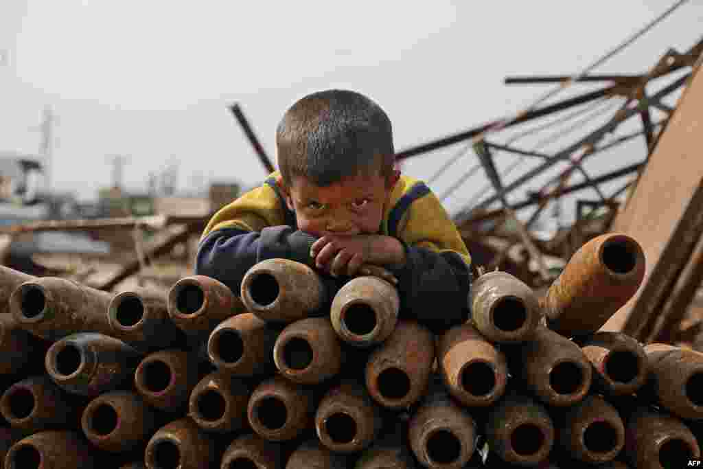 시리아 이들리브 북서쪽 마을의 고철 처리장에 버려진 녹슨 포탄 무더기 위에 아이가 엎드려 있다. 시리아 난민 가족은 4년전 하마에서 전쟁을 피해 탈출한 후 고철을 수거해 생계를 유지하고 있다. 