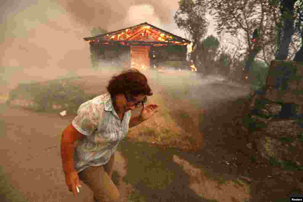 Seorang perempuan berlari menghindar dari rumah yang terbakar di desa Oteiro, dekat Sao Pedro do Sul, Portugal.