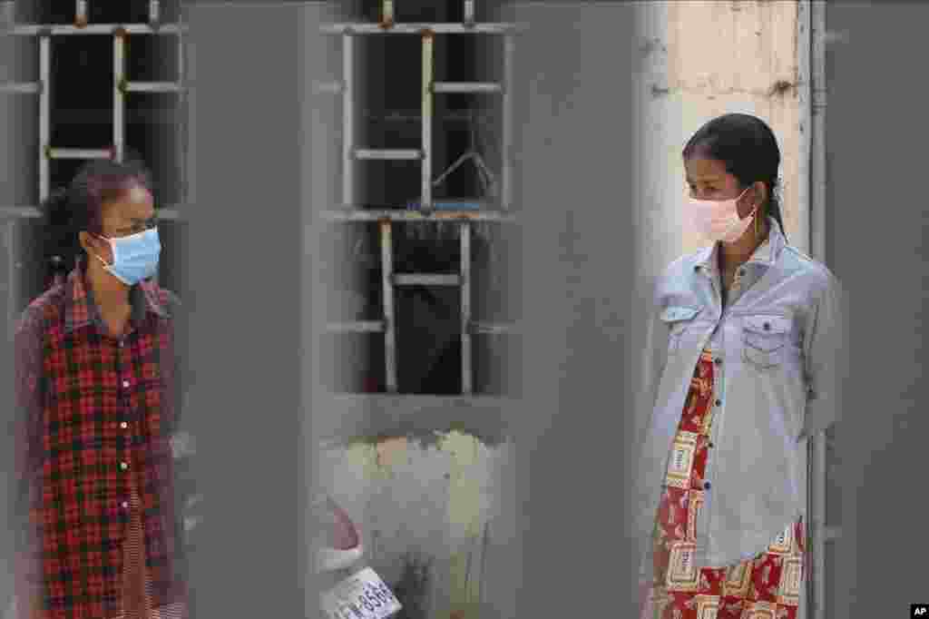 Women in masks watch employees of the non-profit Cambodian Children's Fund spray disinfectant in helping curb the spread of the new coronavirus in the slum neighborhood of Stung Meanchey in southern Phnom Penh, Cambodia, on Tuesday, March 24, 2020. (AP Photo/Heng Sinith)