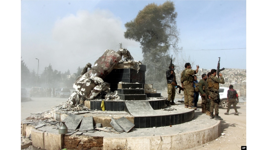 FILE - Turkey-backed Free Syrian Army soldiers celebrate around a statue of Kawa, a mythology figure in Kurdish culture, after destroying it in the city center of Afrin, northwestern Syria, March 18, 2018.