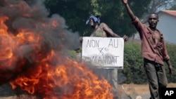 FILE - An opposition demonstrator holds a sign in French reading "No to a third term" next to a barricade fire set by protesters in the Ngagara neighborhood of Bujumbura, Burundi, June 3, 2015.