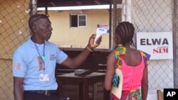 FILE - An unidentified family member, right, of a 10-year-old boy that contracted Ebola, has her temperature measured by a health worker before entering the Ebola clinic were the child is being treated on the outskirts of Monrovia, Liberia, Nov. 20, 2015