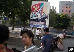 A man sits under a propaganda banner in Pyongyang, North Korea, Aug. 23, 2015.