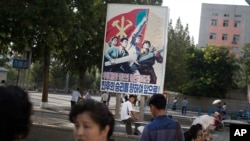 A man sits under a propaganda banner in Pyongyang, North Korea, Aug. 23, 2015. 