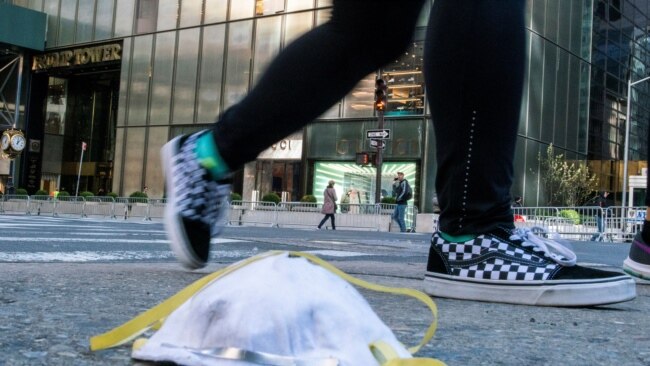 2020年3月14日，一名女子从特朗普大厦附近街面上一个用过的防护口罩旁走过。