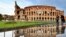 People walk past the Colosseum monument in Rome, reflected in a pool of water following heavy rains.