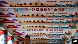 FILE - A man stands underneath the pillars displaying Chinese President Xi Jinping's signature "China Dream" and "One Belt, One Road" foreign policy plan during an event in Beijing, June 29, 2018. 