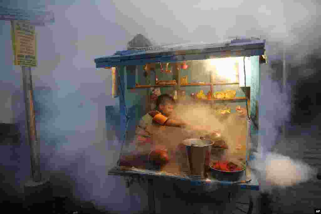 A man covers chewable tobacco as a municipal worker fumigates to prevent mosquitoes from breeding in Lucknow, India.