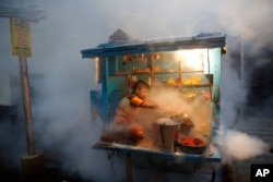 FILE - A man who sells chewable tobacco covers his items as a municipal worker fumigates to prevent mosquitoes from breeding in Lucknow, India, Sept. 22, 2015.