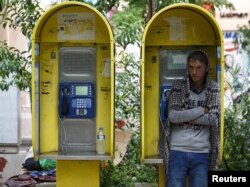 FILE - An Afghan refugee seeks shelter in a phone booth during a rainstorm in Victoria Square, where hundreds of migrants and refugees sleep, in central Athens, Greece, Sept. 21, 2015.