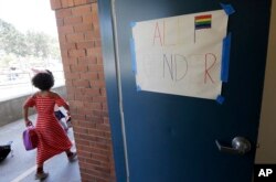 FILE - A camper walks past a sign for an all gender bathroom at the Bay Area Rainbow Day Camp in El Cerrito, Calif., July 11, 2017.