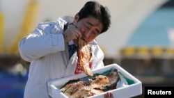 PM Jepang Shinzo Abe menunjukkan bahwa makanan di Fukushima sudah bebas radiasi dengan makan ikan bakar di pelabuhan Soma, Fukushima (foto: dok).