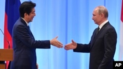 Japan's Prime Minister Shinzo Abe, left, and Russia's President Vladimir Putin reach out to shake hands during a press conference after the G-20 summit in Osaka, Japan, June 29, 2019.