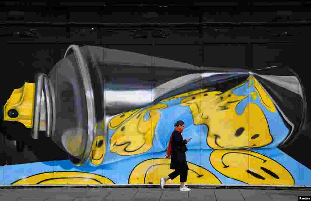 A woman views her phone as she walks past street art on a wall in London, Britain.