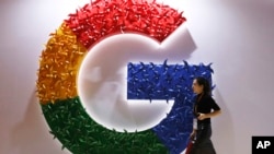 FILE - A woman walks past the logo for Google at the China International Import Expo in Shanghai, Nov. 5, 2018.