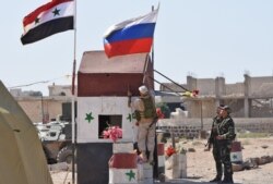 FILE - A Russian soldier places the national flag at the Abu Duhur crossing on the eastern edge of Idlib province, Sept. 25, 2018.