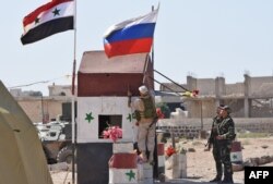 FILE - A Russian soldier places the national flag at the Abu Duhur crossing on the eastern edge of Idlib province, Sept. 25, 2018.