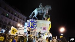 Para pengunjuk rasa menempatkan spanduk di patung Raja Carlos III sebagai bagian dari protes anti langkah penghematan di Puerta del Sol Plaza, Madrid, Sabtu (12/5).