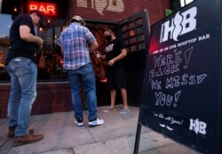 FILE - Handlebar bouncer, Mando Cuadros, sprays down a guest's hands with hand sanitizer on the first night that bars reopen after they were shut down to stop the spread of the coronavirus disease (COVID-19) in Austin, Texas, May 22, 2020.