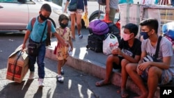 A young boy and girl hold hands as they arrive with their parents to try to catch a ride at the Cubao bus terminal in Manila, Philippines on Friday, March 13, 2020. 