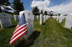 A flag stands next to the gravestone for a U.S. World War II veteran, at Fort Logan National Cemetery, in Sheridan, Colorado, May 23, 2020.