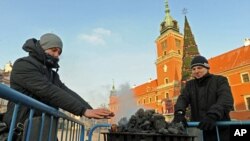 Passersby warm hands near a charcoal heater in front of the Royal Castle in Warsaw, Poland, Feb. 2, 2012.