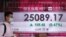A man wearing a face mask walks past a bank's electronic board showing the Hong Kong share index at Hong Kong Stock Exchange, July 20, 2020. 