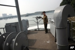 FILE - A North Korean guide poses near a machine gun on the spy ship USS Pueblo, now a tourist attraction in Pyongyang.