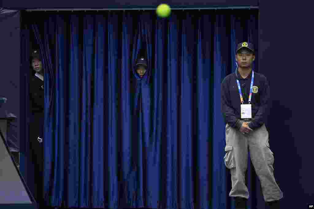 Workers look through curtains to watch a match between France&#39;s Gael Monfils and Russia&#39;s Daniil Medvedev during the China Open tennis tournament held at the National Tennis Center in Beijing.