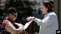 In this photo taken Monday, June 10, 2019, Seattle City Council candidate Pat Murakami, right, looks on as voter Lashaun Hartfield signs a voucher for Murakami's campaign in Seattle. (AP Photo/Elaine Thompson) 