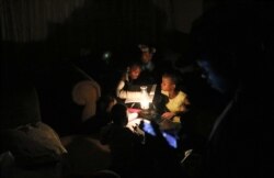 FILE - Children use a parafin light to study during an electricity load-shedding blackout in Soweto, South Africa, March 18, 2021.