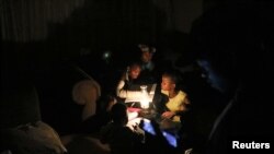 FILE - Children use a parafin light to study during an electricity load-shedding blackout in Soweto, South Africa, March 18, 2021.