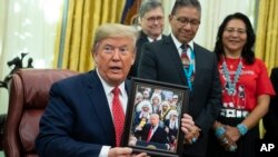 President Donald Trump shows off a gift during and event to sign an executive order establishing the Task Force on Missing and Murdered American Indians and Alaska Natives, in the Oval Office of the White House, Nov. 26, 2019, in Washington. 