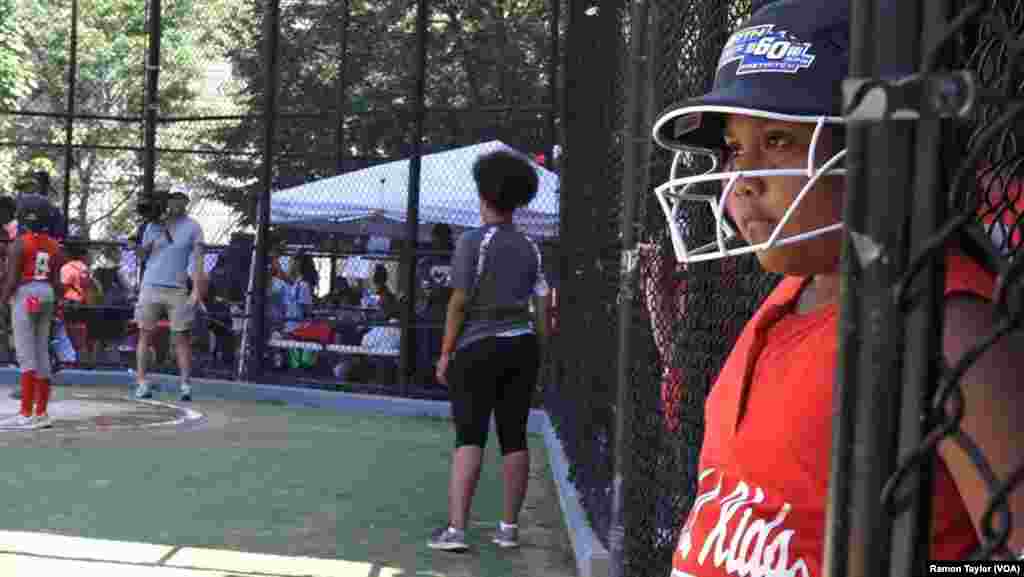A young softball player on the South Bronx Red Wings awaits her turn at the dugout at the Harlem RBI field, in New York, Aug. 12, 2016.