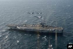 In this Nov. 10, 2017, photo provided by Japan's Air Self-Defense Force, two U.S. F/A-18s and a Japanese F-15 fly over the USS Ronald Reagan toward a joint military exercise at an undisclosed location.