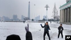 Niños norcoreanos juegan con nieve en la Plaza Kim Il Sung, en Pyongyang, el domingo 16 de diciembre de 2018, al inicio de la temporada invernal, al fondo la Torre 'The Juche Idea'.