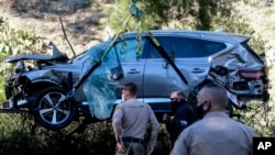 Law enforcement officers watch as a crane is used to lift a vehicle following a rollover accident involving golfer Tiger Woods, Tuesday, Feb. 23, 2021, in the Rancho Palos Verdes section of Los Angeles. (AP Photo/Ringo H.W. Chiu)