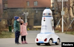 FILE - Children react next to a security robot patroling inside a residential compound in Hohhot, Inner Mongolia, China, Jan. 18, 2019.