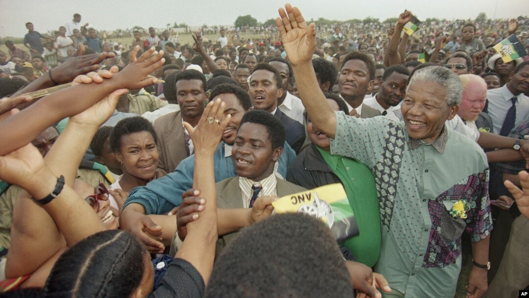 African National Congress President Nelson Mandela, right, waves to the gathered crowd at Jouberton Township stadium as people reach out to touch him during a campaign rally on Jan. 30, 1994.