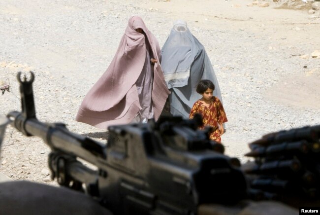 Perempuan Afghanistan berpakaian burqa dan seorang gadis berjalan melewati kantor polisi setempat di kota Kandahar, Afghanistan selatan, 22 Maret 2010. (REUTERS/Shamil Zhumatov)