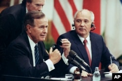 FILE - U.S. President George H. Bush works to get an earphone plug from his ear as Soviet President Mikhail Gorbachev laughs during their joint news conference, Sept. 9, 1990, in Helsinki.