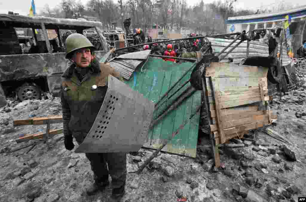 A protester holds a riot police shield in front of barricade after violent clashes in central Kyiv, Ukraine.