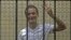 FILE - Egyptian activist Ahmed Douma gestures from behind bars at the New Cairo court, on the outskirts of Cairo.