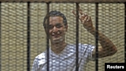 FILE - Egyptian activist Ahmed Douma gestures from behind bars at the New Cairo court, on the outskirts of Cairo.