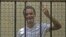 FILE - Egyptian activist Ahmed Douma gestures from behind bars at the New Cairo court, on the outskirts of Cairo.