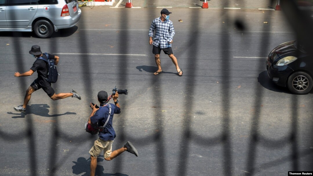 Pro-democracy protesters and a journalist run as riot police officers advance them during a rally against the military coup in Yangon