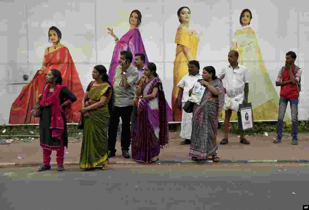 Indians returning after the day&#39;s work await bus transport standing on a pavement next to an advertisement hoarding of a clothing store in Thiruvananthapuram, Kerala state, India.