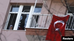 A woman looks through a damaged window in her home, close to the site of Wednesday's suicide bomb attack in Ankara, Turkey, Feb. 19, 2016.